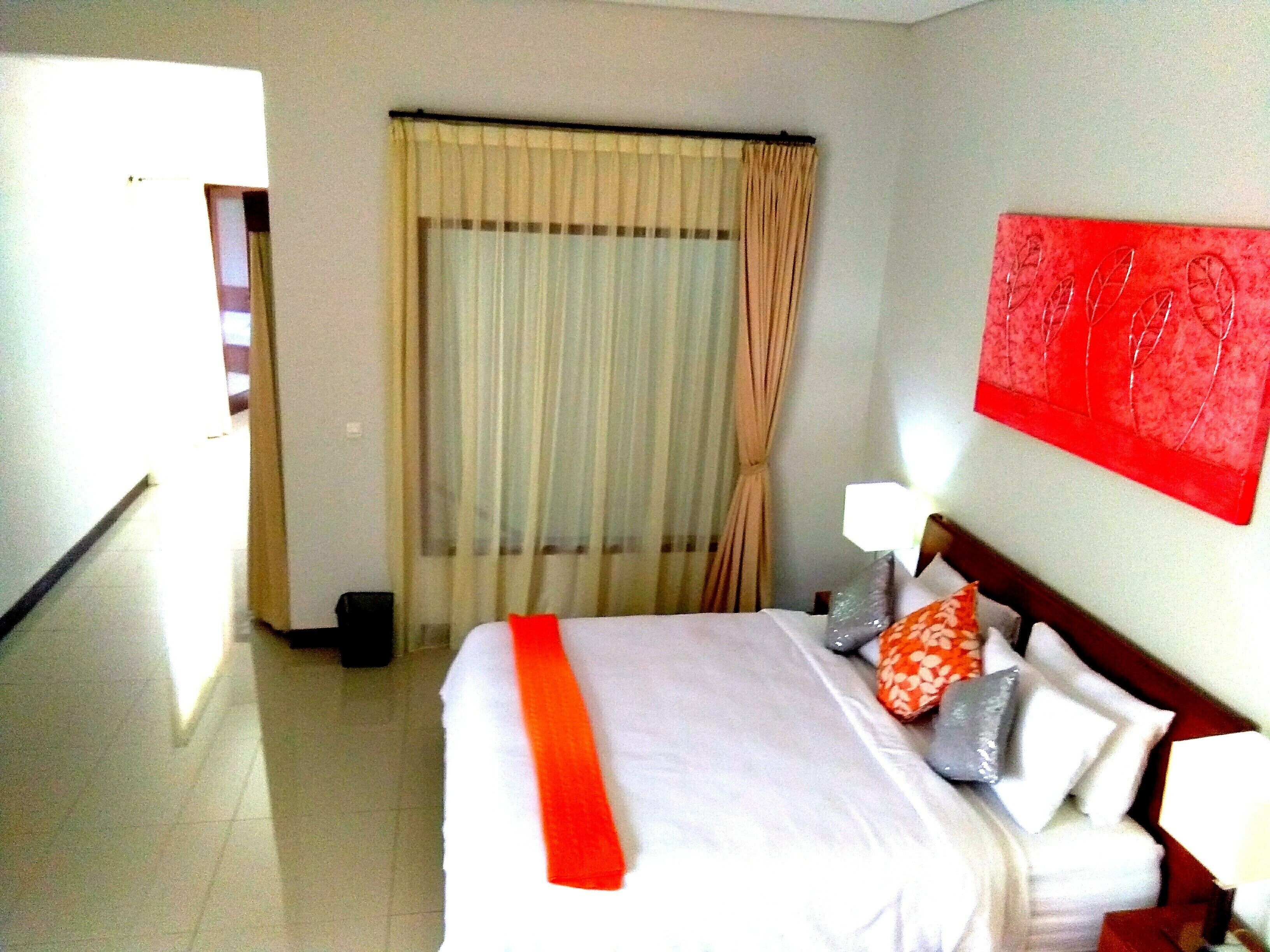 A hotel room with a bed, curtains, a red wall decoration, and a nightstand.