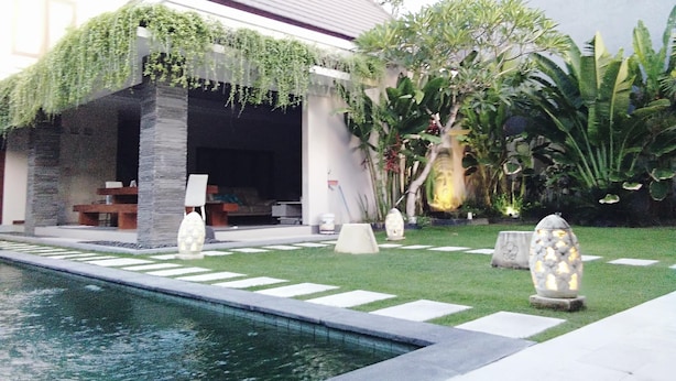 A modern building with a pool, stone pillars, and lush greenery. - Gathering With 5 Bedroom Center House Villa (Legian)
