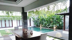 An outdoor dining area with a pool, surrounded by lush greenery and a tiled patio. - Gathering With 5 Bedroom Center House Villa (Legian)