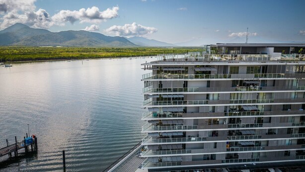 A multi-story hotel with balconies overlooking a calm lake, surrounded by lush greenery and mountains.