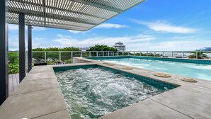 A rooftop infinity pool with a hot tub, surrounded by a covered area with a view of the city skyline.