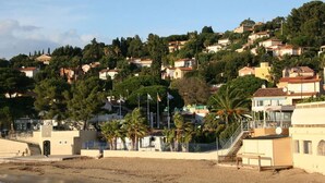 Une ville côtière avec des bâtiments construits sur une colline, une plage et des palmiers.