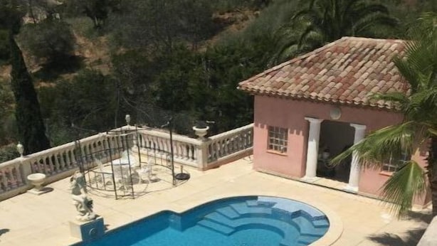 Une piscine avec une terrasse carrelée, un petit pavillon et une statue.