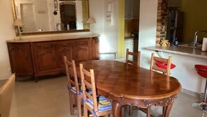 Un coin repas avec une table et des chaises en bois, une cuisine en arrière-plan et un grand miroir au-dessus de la table.