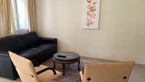 Un salon avec un canapé noir, deux fauteuils beige, une petite table ronde et un élément décoratif mural.