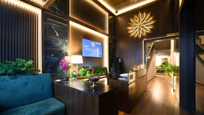 Una hall d'albergo moderna con una reception, un divano blu e un grande cartello illuminato.
