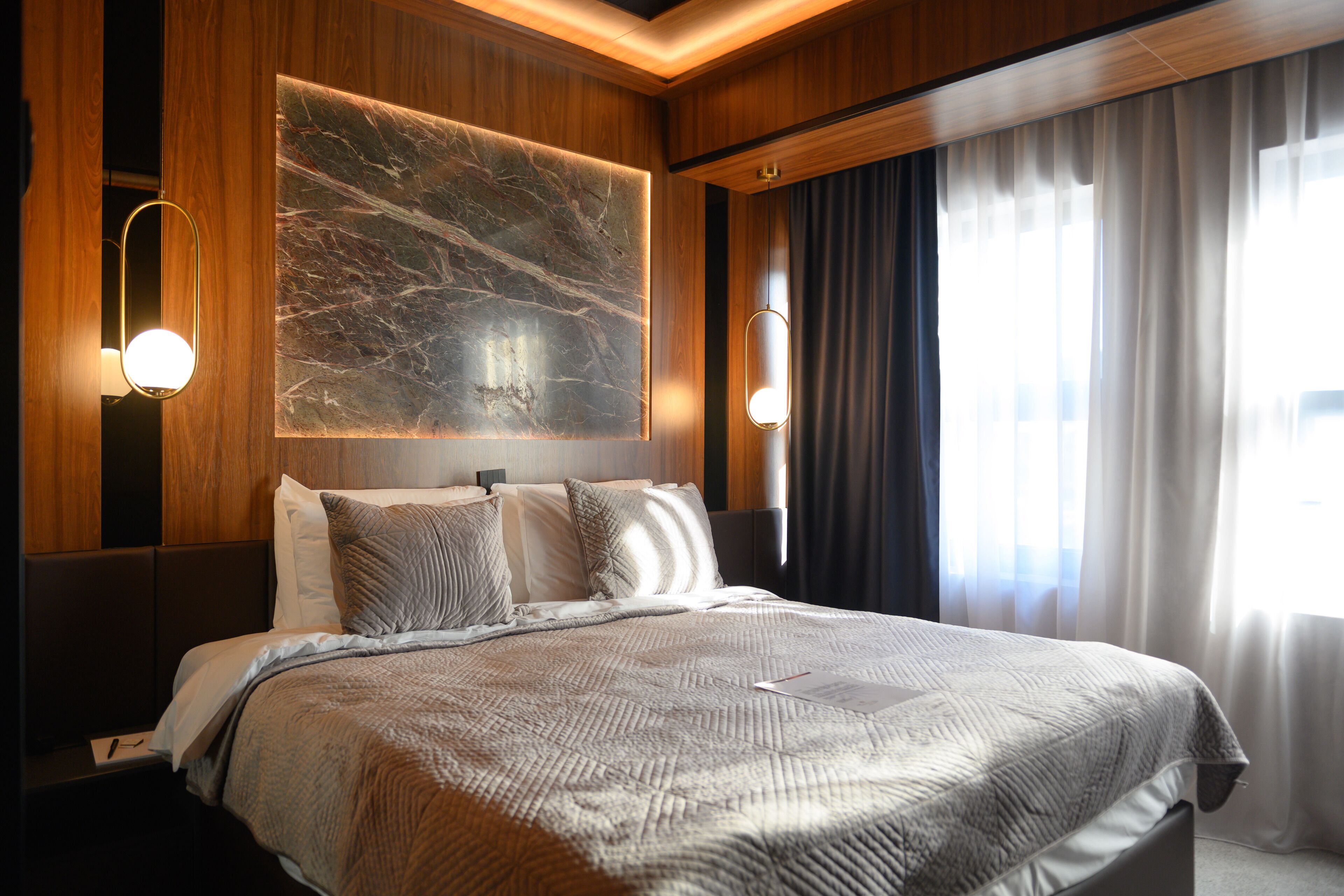 A hotel room with a large bed, wooden paneling, a marble accent wall, and two wall-mounted lights.