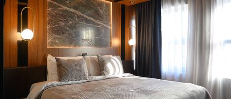 A hotel room with a large bed, wooden paneling, a marble accent wall, and two wall-mounted lights.