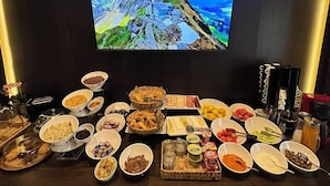 Un tavolo per buffet con diversi cibi e un televisore che mostra un paesaggio montano.