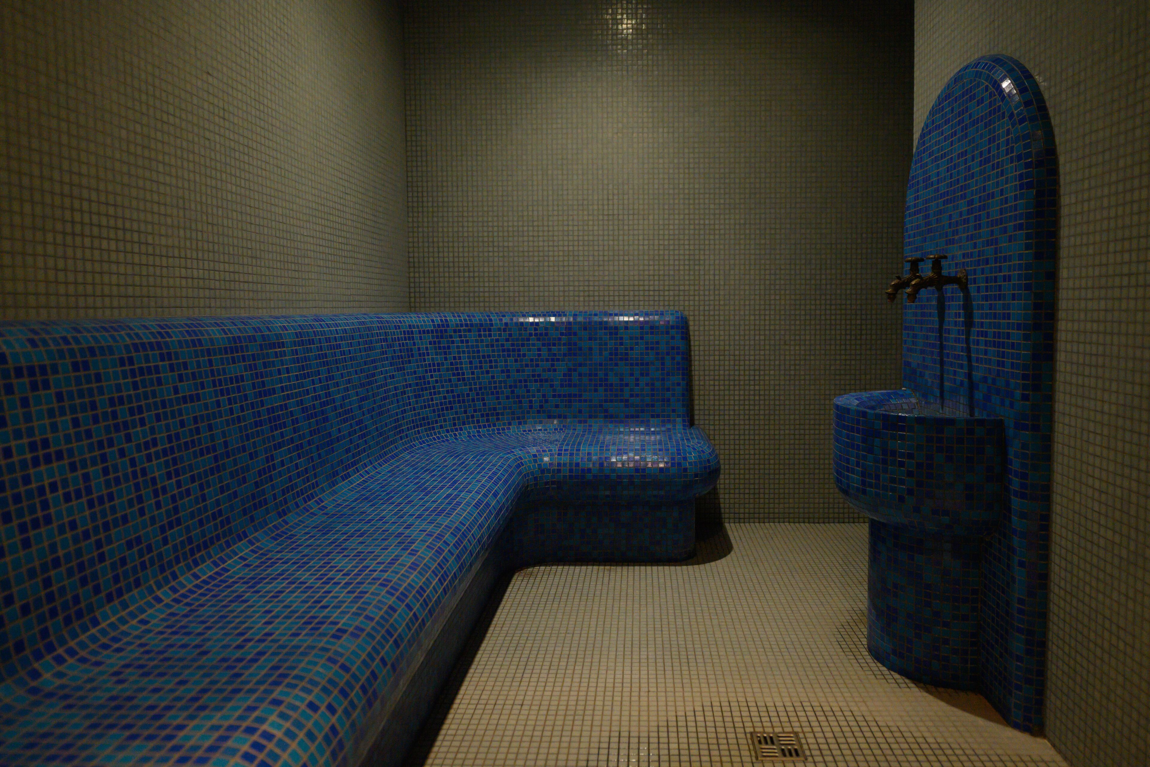 Un baño con una bañera de mosaico azul, inodoro y lavamanos empotrado.