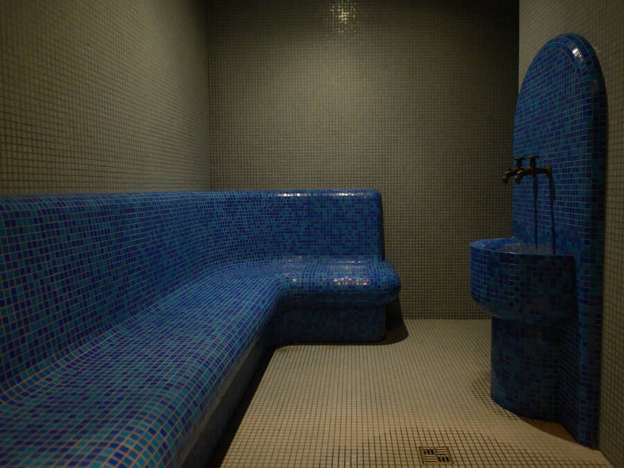 Een badkamer met een blauw mozaïekbad, een toilet en een wandfontein.