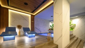 Un'area benessere con pavimento in legno, due poltrone imbottite blu, una piccola piscina e una scalinata.