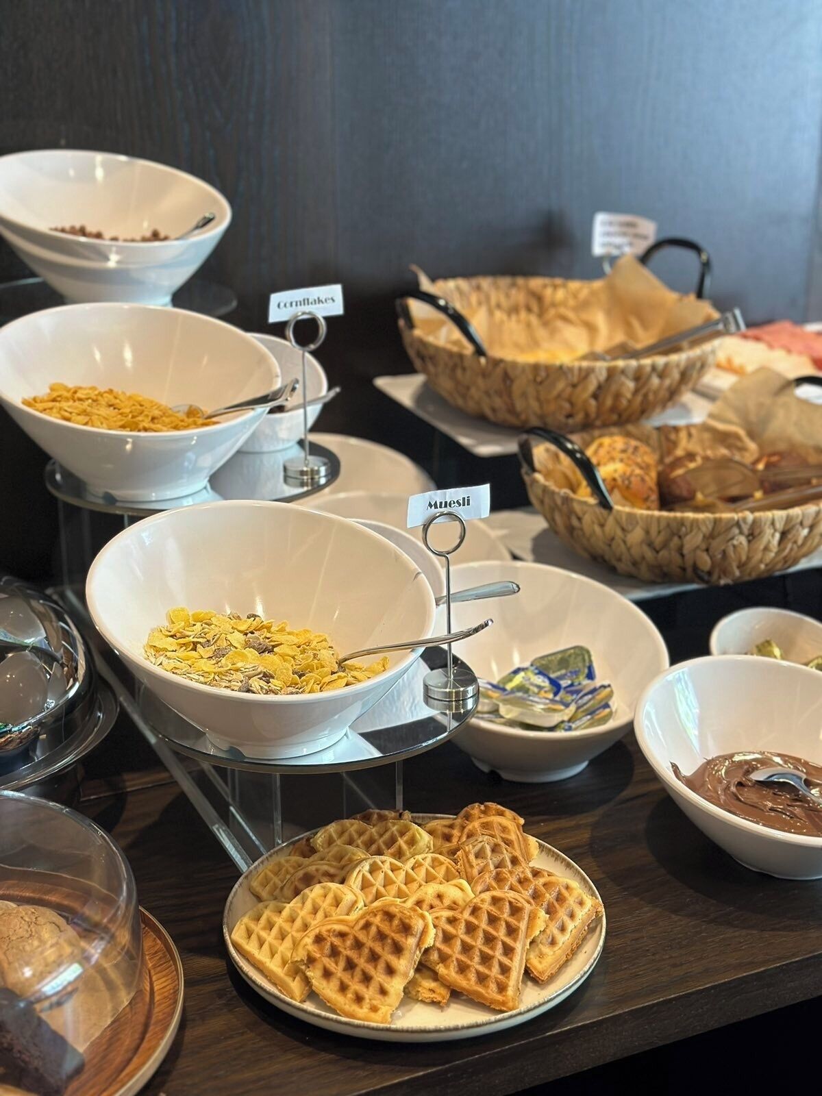 A buffet with various food items including cereal, waffles, and pastries.