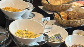 A buffet with various food items including cereal, waffles, and pastries.