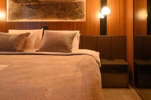 Una cama bien tendida con una colcha y almohadas estampadas, un adorno de pared tipo mármol encima, y una mesita de noche con una lámpara.