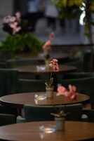 Interior de restaurante con mesas redondas, sillas tapizadas de color verde y plantas en macetas.
