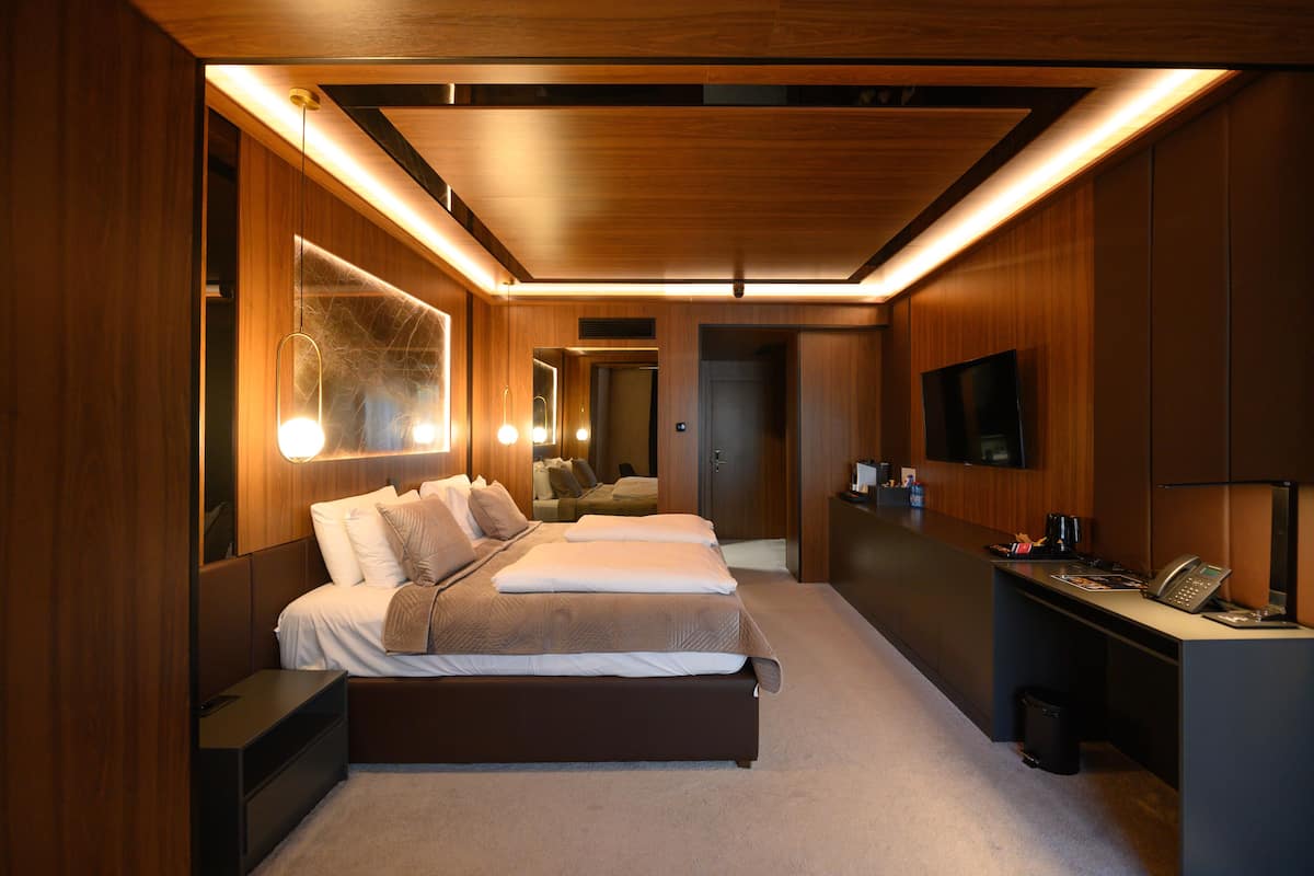 A modern hotel room with a large bed, bedside tables, a desk with a computer, and a TV.