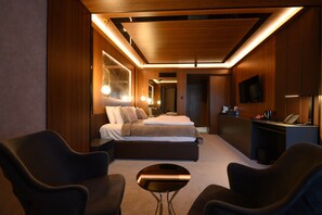 Et moderne hotelværelse med en seng, to lænestole, et lille bord, et skrivebord med en telefon og et fjernsyn på væggen.