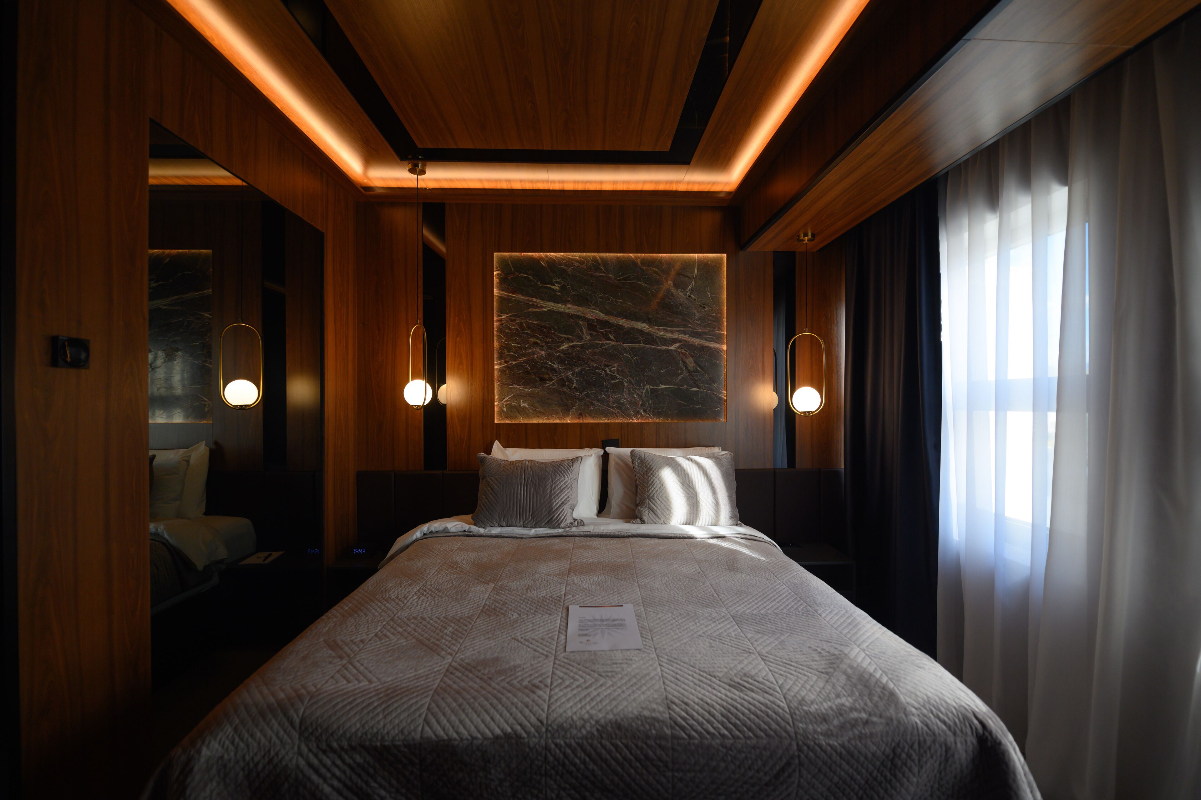 A hotel room with a large bed, wooden paneling, a marble wall art piece, and two bedside lamps.