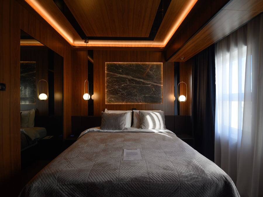 Una habitación de hotel con una cama grande, paneles de madera, una obra de arte de mármol en la pared y dos lámparas de noche.