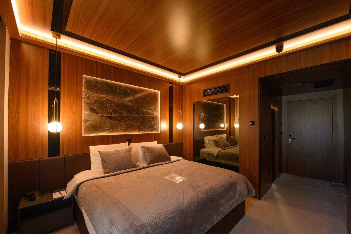 A modern hotel room with a large bed, wooden paneling, and a large abstract artwork above the bed.