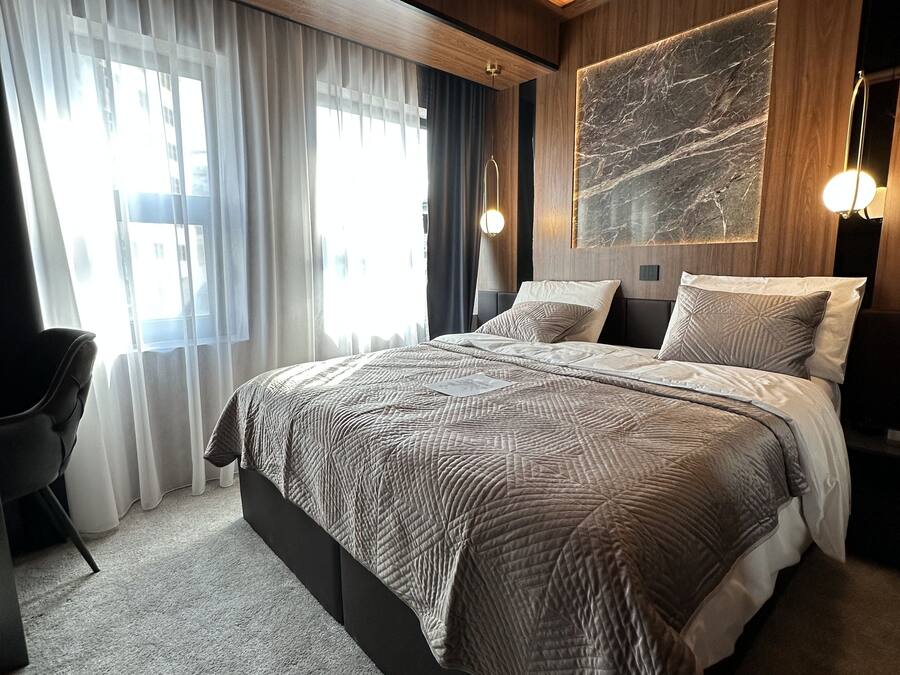 A modern bedroom with a large bed, a desk, and a view of the city.