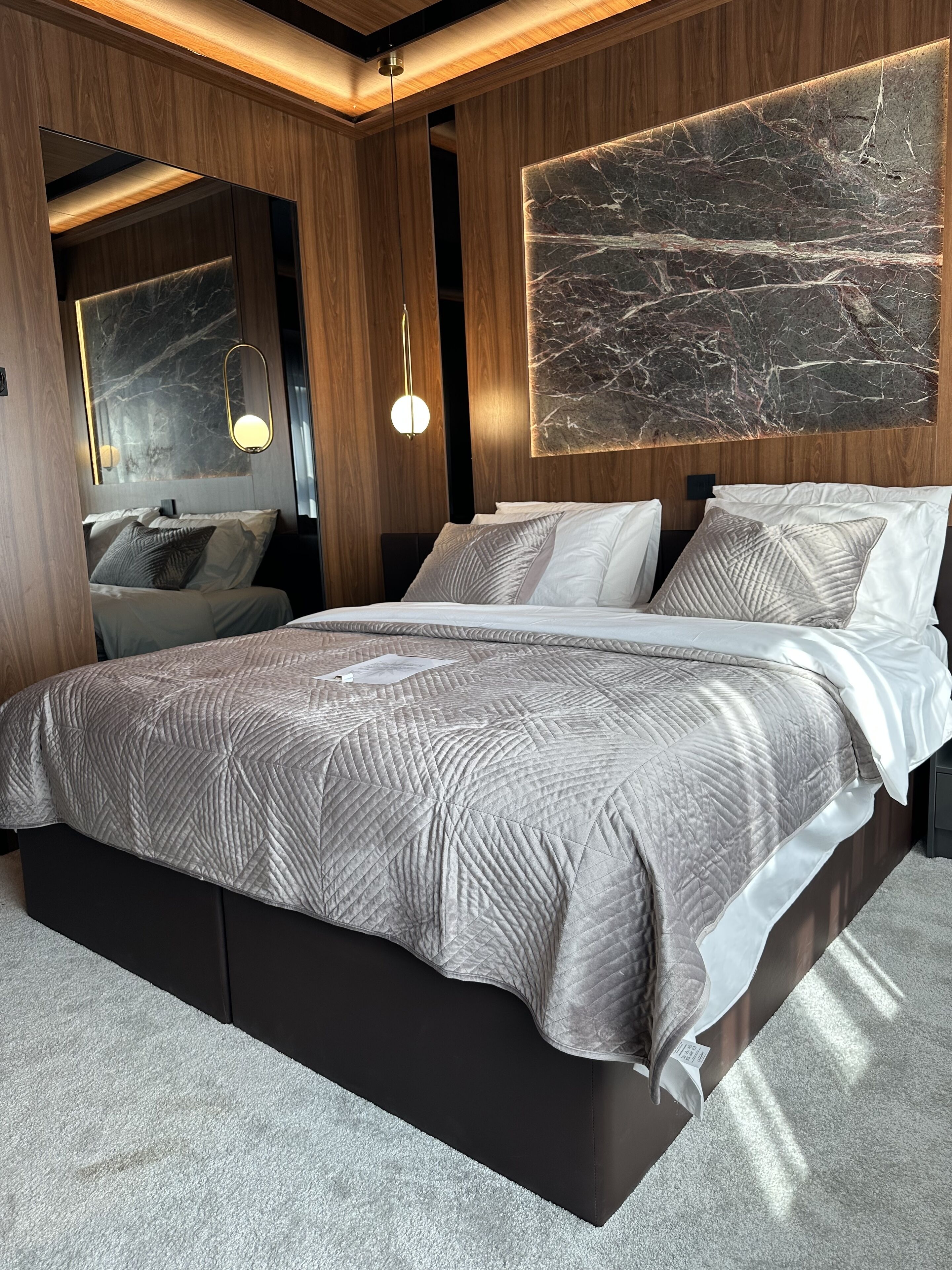 A modern bedroom with a large bed, wooden paneling, a marble wall, and a pendant light.