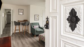 Een moderne woonkamer met een grijze bank, twee bijpassende fauteuils, een kleine tafel en een kleurrijk plaid. Een witte deur met een zwart bloemenpatroon is zichtbaar.