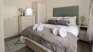 Een slaapkamer met een bed, een dressoir, een nachtkastje, een spiegel en een hanglamp.