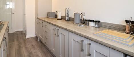 A modern kitchen with grey cabinets, a wooden countertop, and various appliances.
