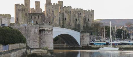 Uma ponte de pedra histórica sobre um rio calmo, que leva a um castelo com várias torres.
