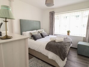 A neatly arranged bedroom with a bed, bedside table, lamp, and a window with curtains. - The Old Coach House (Conwy)