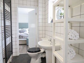 A modern bathroom with white tiles, a black toilet, a sink, and a shelf with a towel. - The Old Coach House (Conwy)
