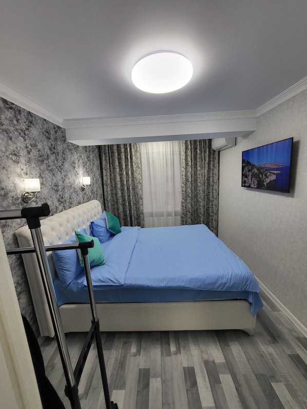 A bedroom with a bed, a headboard, a nightstand, a lamp, a painting, and a window with curtains.