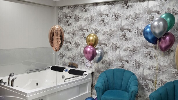 Ein modernes Badezimmer mit einer großen Badewanne, zwei türkisfarbenen Sesseln und bunten Luftballons.