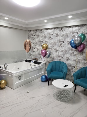 Un baño moderno con una bañera grande, dos sillones color turquesa y globos de colores.