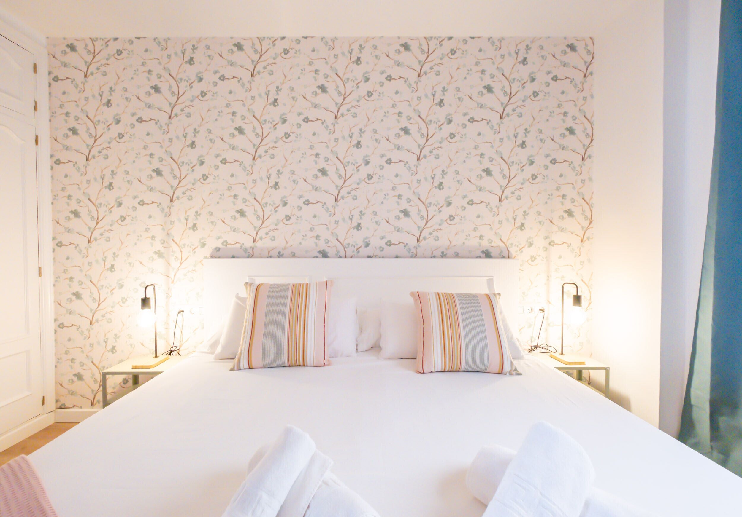 A hotel room with a large bed, two bedside tables with lamps, and a floral wallpaper pattern.