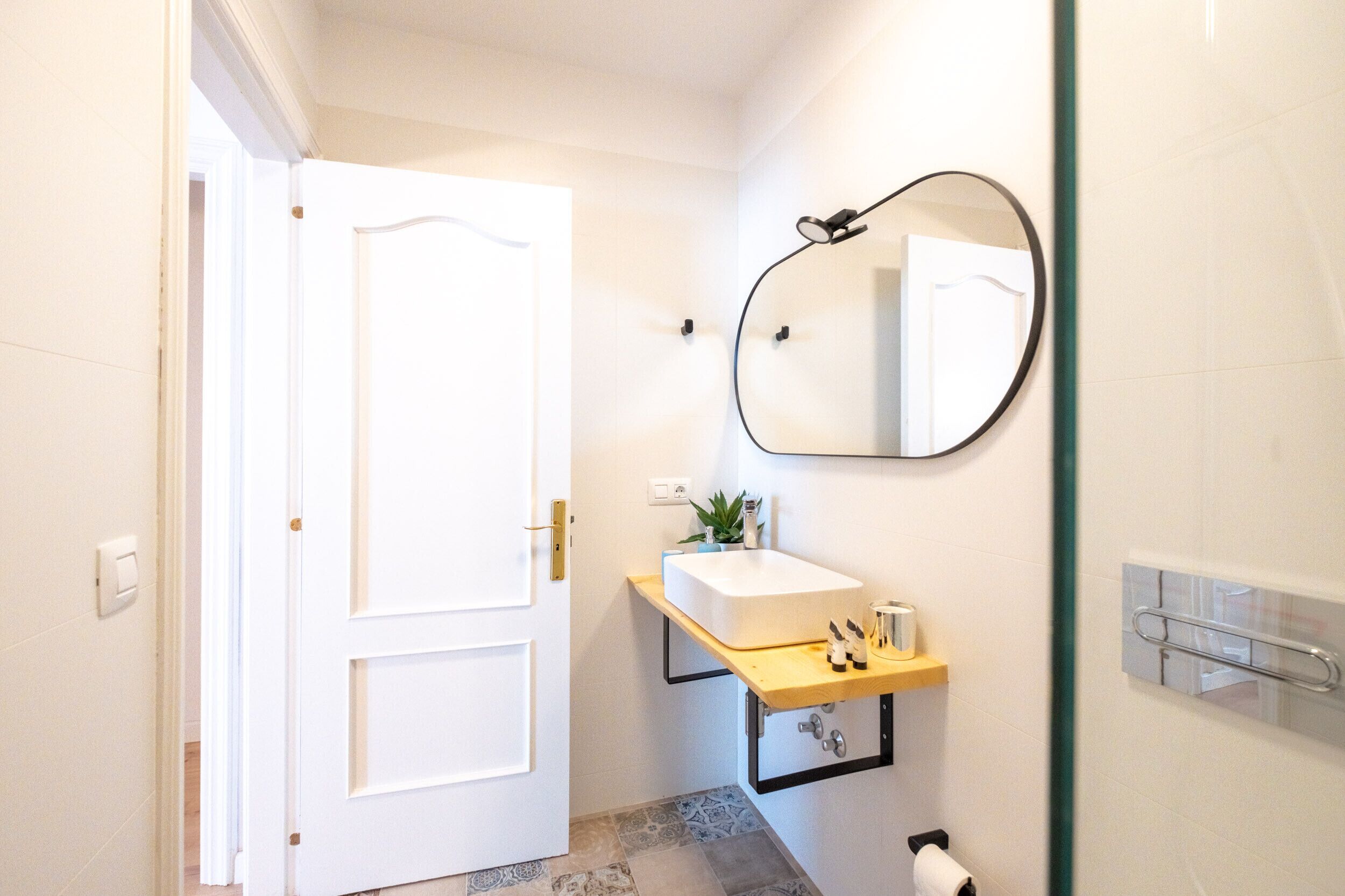 Une salle de bain avec une porte blanche, un lavabo surmonté d’un miroir et un porte-serviettes fixé au mur.