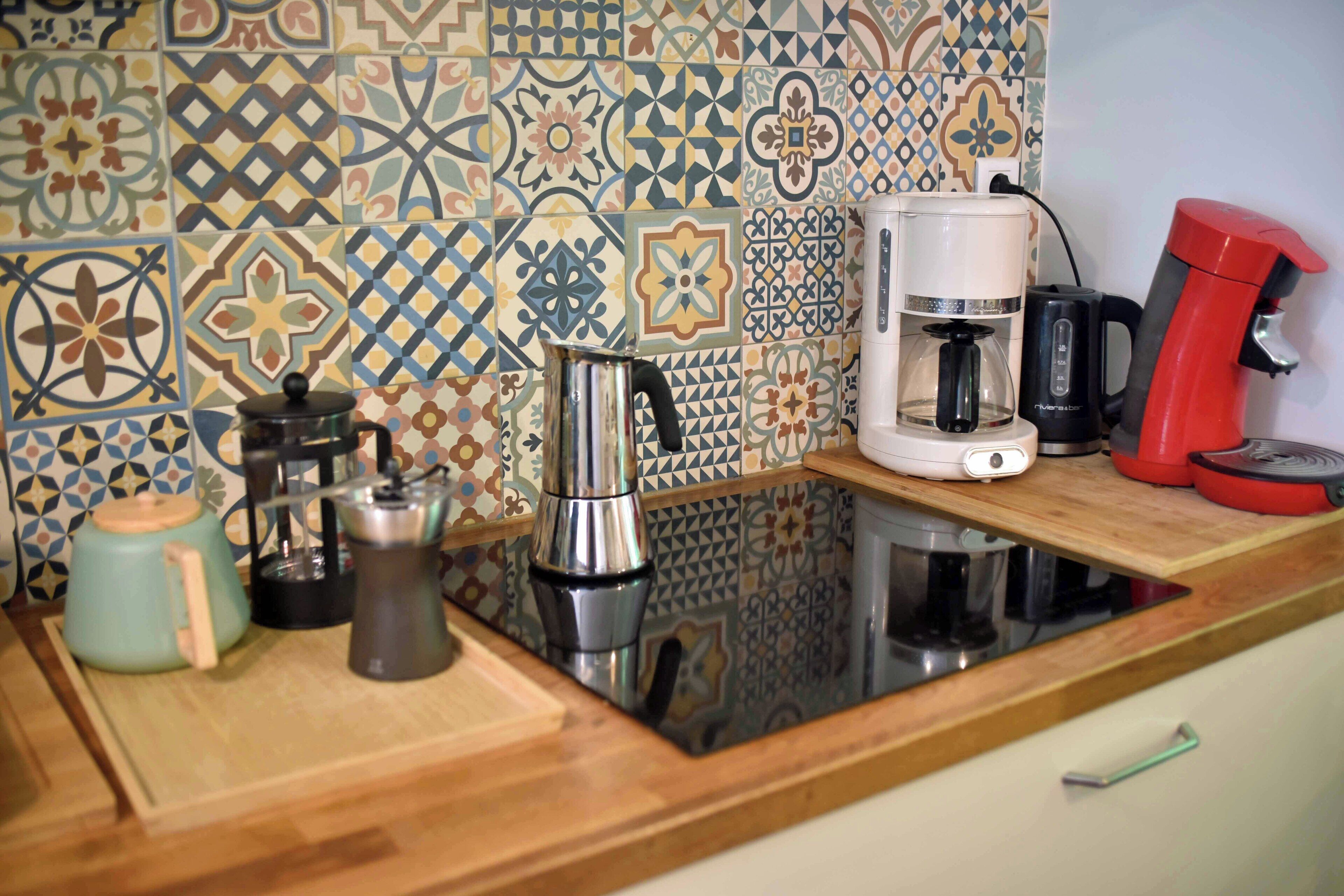 Een keuken met een koffiezetapparaat, een waterkoker en een rode koffiemolen op het aanrecht.