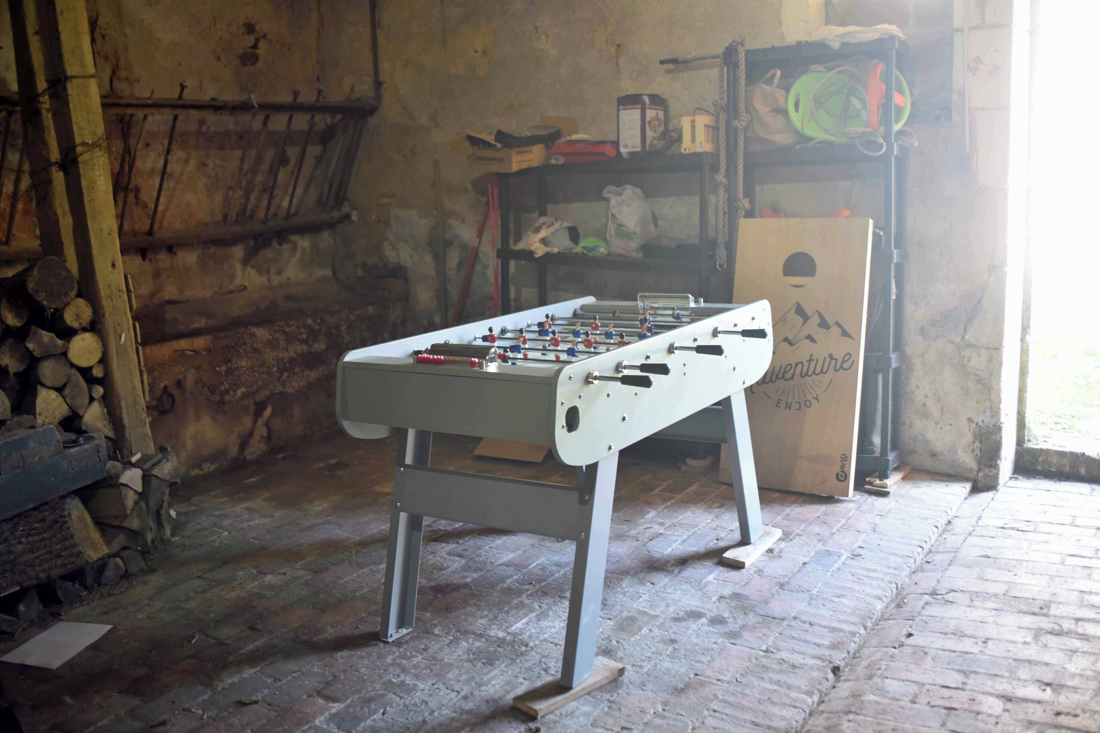 A foosball table in a rustic room with brick flooring and wooden walls.