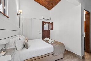 A hotel room with a bed, a bedside table with a phone, a wall-mounted air conditioner, a window with a view, and a wooden ceiling.