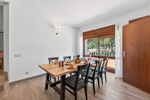 Ein Essbereich mit Holztisch und -stühlen, einem Fenster mit Blick auf Bäume und einer Tür rechts.