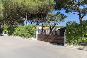 A quiet residential street with a wooden fence, lush green trees, and a clear blue sky. - Casa da Aldeia | 4 Bedrooms | Next to Pine Cliffs | Olhos de Água (Albufeira)