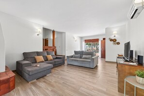 Ein modernes Wohnzimmer mit zwei grauen Sofas, einem Holztisch und einer TV-Bank mit Lautsprechern.
