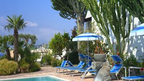 A pool area with blue lounge chairs and umbrellas, surrounded by cacti and palm trees. - "room in B&B - Ischia, Forio With a Breathtaking View, Above the Poseidon Gardens for 5 People" (Forio)