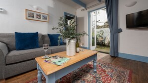 Ett vardagsrum med en grå soffa, blå kuddar, ett träbord med tidningar, en vit vas med en växt och en blå gardin.