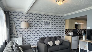 Ein modernes Wohnzimmer mit einem grauen Sofa, einem kleinen Beistelltisch und einer Wand mit Muster.