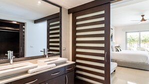 A modern bathroom with dual sinks, a large mirror, and a sliding door leading to a bedroom with a bed and a ceiling fan. - Casa Lucerna Splash Pool Unit,Where the Caribbean feels like home (Playa del Carmen)
