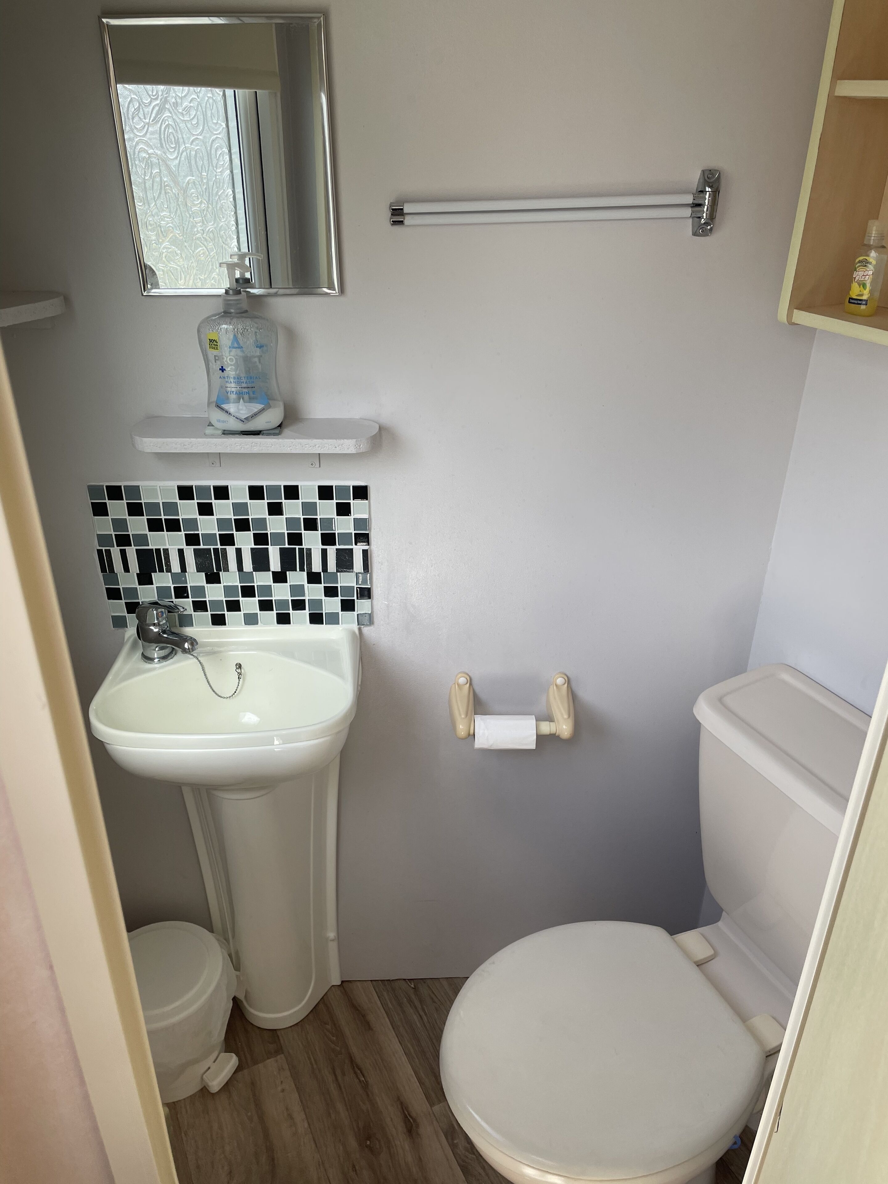 A bathroom with a white sink, a toilet, a mirror, and a shelf with a bottle.