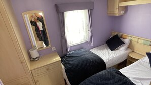 Une chambre de taille modeste, comprenant deux lits, un miroir, une fenêtre avec des rideaux, un petit bureau et un radiateur.